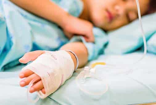 Child with a IV in his hand laying in a hospital bed